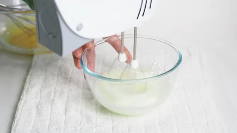 A man beats egg white with a mixer in a transparent bowl in the kitchen. Several Stock Footage 231726077