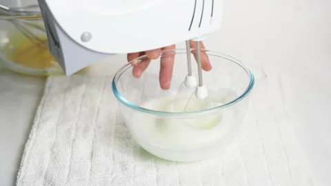 A man beats egg white with a mixer in a transparent bowl in the kitchen. Stock Footage 231865050