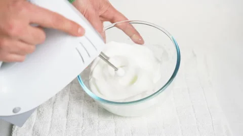 A man beats egg white with a mixer in a transparent bowl in the kitchen. Stock Footage 231865307