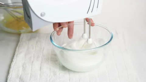 A man beats egg white with a mixer in a transparent bowl in the kitchen. Stock Footage 231865643