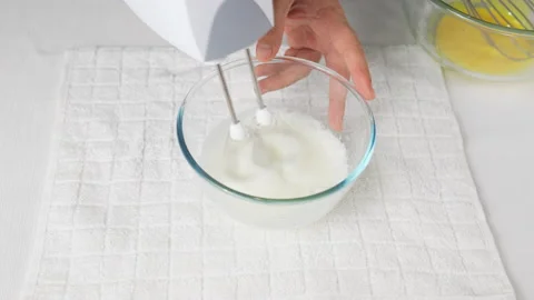 A man beats egg white with a mixer in a transparent bowl in the kitchen. Stock Footage 231865907