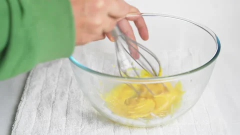 A man beats eggs with a hand whisk in a transparent bowl on the kitchen table Stock Footage 231707780