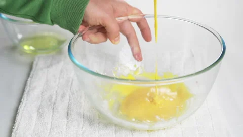 A man beats eggs with a hand whisk in a transparent bowl on the kitchen table Stock Footage 231708009