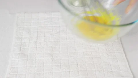 A man beats eggs with a hand whisk in a transparent bowl on the kitchen table Stock Footage 231708261