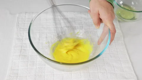 A man beats eggs with a hand whisk in a transparent bowl on the kitchen table Stock Footage 231708718
