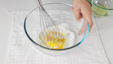 A man beats eggs with a hand whisk in a transparent bowl on the kitchen table Stock Footage 231709593