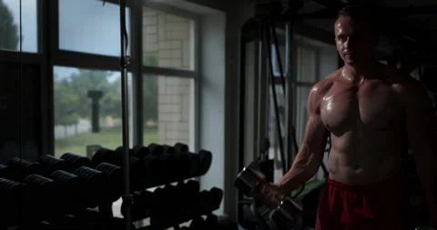 A man with a beautiful torso standing in front of a mirror raises dumbbells Stock Footage 158922036