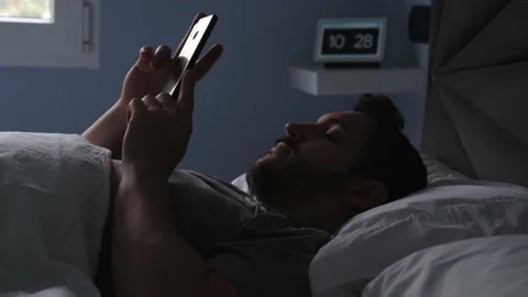 Man in bed asking a digital assistant to turn on the light Stock Footage