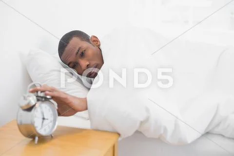 Man in bed extending hand to alarm clock Stock Photos
