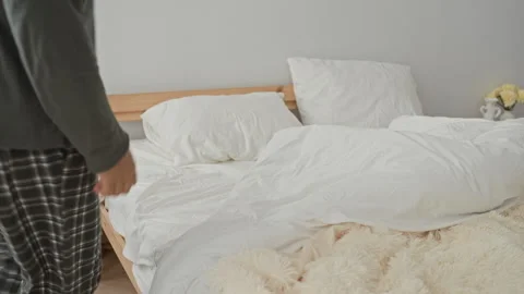 Man on bed pulls duvet over face and grips pillow in a small bedroom inside.. Stock Footage 339164860