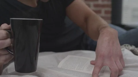 Man on bed reading a book and drinking coffee Stock Footage 70808289