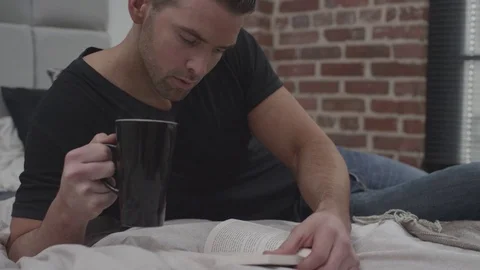 Man on bed reading a book and drinking coffee Stock Footage 70808717