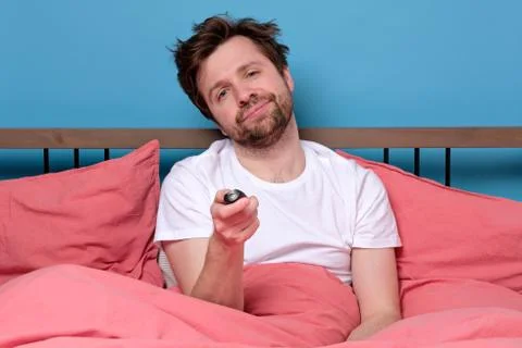 Man in bed using remote control for changing tv channel or air conditioning f Stock Photos