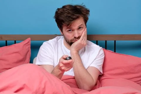 Man in bed using remote control for changing tv channel or air conditioning f Stock Photos