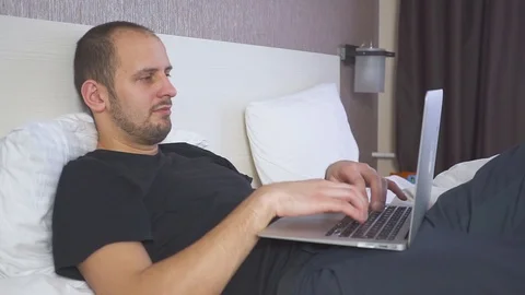 Man in Bed Working on Laptop and really want to sleep, rubs his eyes. Stock Footage 100867601