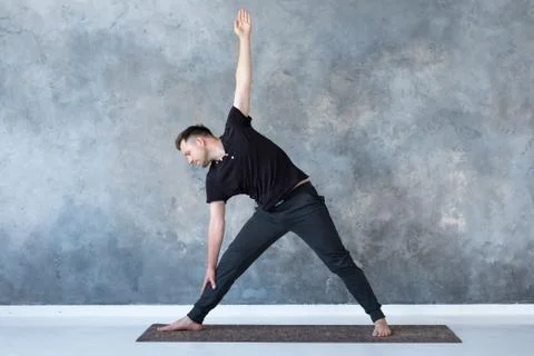 Man beginner practicing yoga doing trikonasana pose. Stock Photos