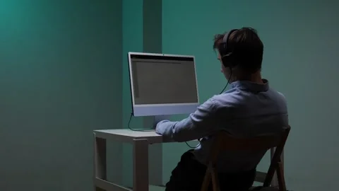 Man from behind concentrating at a computer screen while wearing headphones Stock Footage 345530072