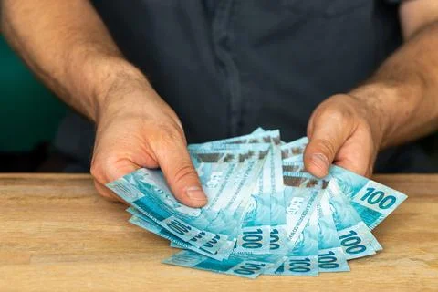 The man behind the desk is holding a bundle of one hundred reais Brazilian .. Stock Photos