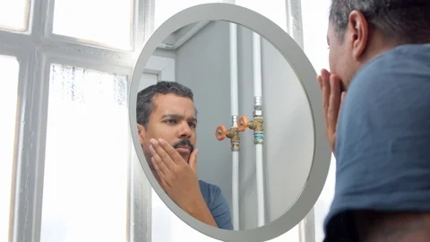 Man behind the mirror during his morning facial care routine watching at himself Stock Footage 127039612