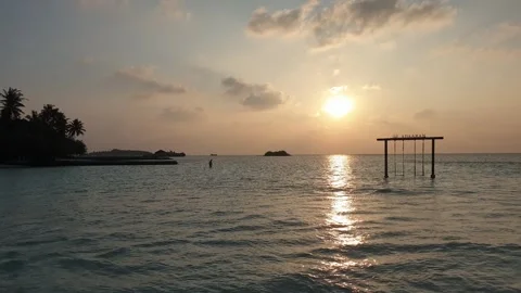 Man behind swing walks in ocean of maldives at dusk Stock Footage 280794912