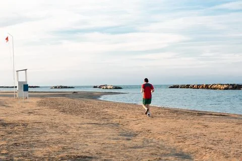 Man from behind training on the empty beach at sunset. Fitness man doing running Stock Photos