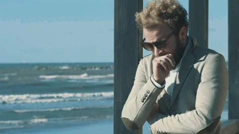 Man in beige jacket sitting sadly on a beach terrace Stock Footage 279169488