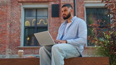 Man being focused on creating of own resume using laptop while sitting outside Stock Footage 250074763