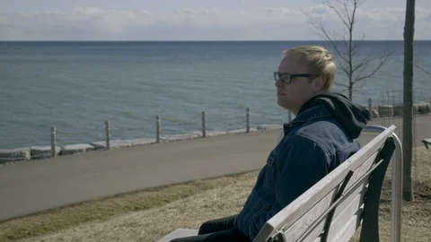 Man on bench looking at the lake while another man drives by on his Stock Footage 105489469