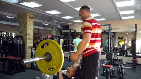 Man bench press bench in the gym, the trainer monitors the performance of the ex Stock Footage 85954296