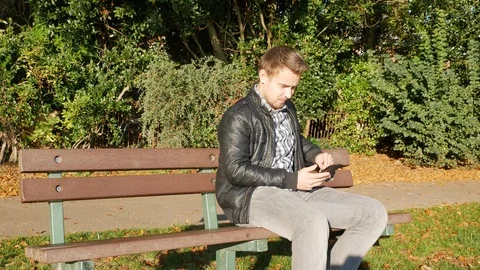 Man on a bench texting on a mobile phone Video stock 97009839