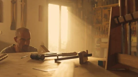 Man bending down while sawing wood with handsaw in workshop Stock Footage 275630184