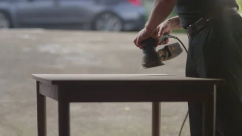 Man bends down while sanding the a wooden table with an electric sander Stock Footage 134288844