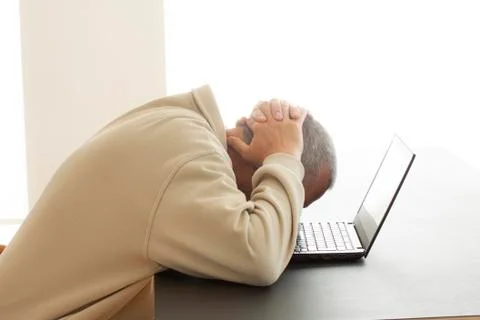 A man bends his head over computer in despair Stock Photos