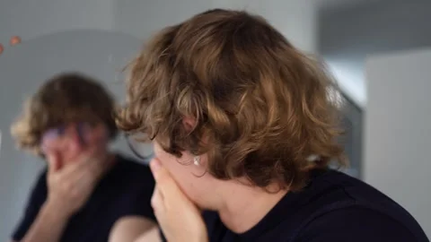 Man bends over and covers his mouth in front of the mirror reacting with intense Vídeo Stock 312981828