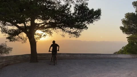 Man with a bicycle overlooking a beautiful mountain lanscape at sunset Stock Footage 283552060