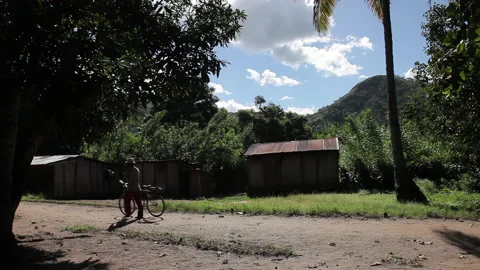 Man with a Bicycle Passing by a Rustic Corrugated Iron Hut in Rural Setting Stock Footage 221130853