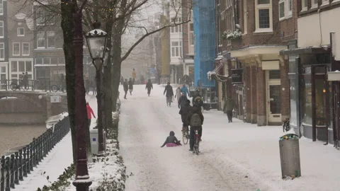 Man on a bicycle pulling a sled with child during snowfall on canal in Amsterdam Stock Footage 148270717