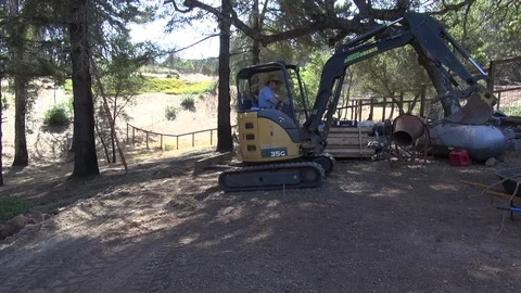 Man in big hat compacting dirt with small front end loader, wide shot, HD Stock Footage 123552013