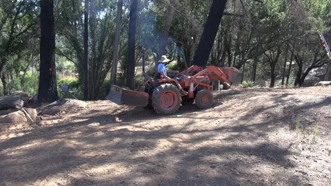 Man in big hat using digger to carry dirt up incline, wide, HD Stock Footage 123550884