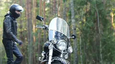 Man biker in a helmet sits down on a motorcycle in the forest at sunset Stock Footage 107657172