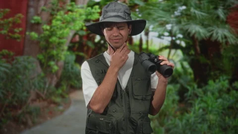 Man with binoculars touching his neck and wincing on a forest path in a bot.. Stock Footage 339197180