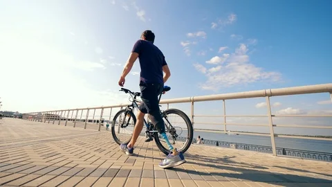 A man with a bionic leg is wheeling a bike along the quay Stock Footage 116801247