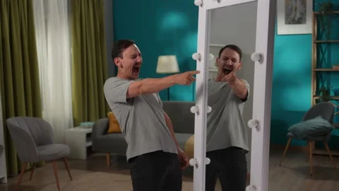 A man with bipolar disorder at a mirror in the living room. The man is writhing Stock Footage 257793482