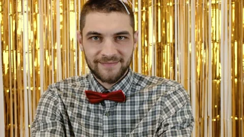 Man in a birthday hat and red bow tie invites with a finger and then offers a Stock Footage 342619666