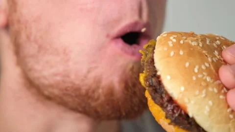 The man bites and chews double cheeseburger. A man eats fast food. Unhealthy Stock Footage 218614411