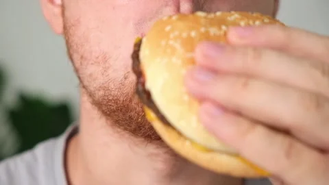 The man bites and chews double cheeseburger. A man eats fast food. Unhealthy Stock Footage 219732101