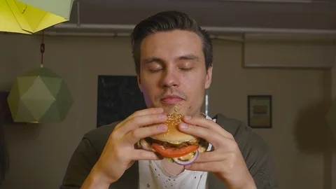 Man bites and eats burger at a restaurant Stock Footage 76162595