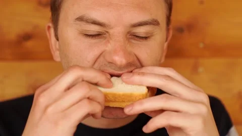 A man bites and eats a sandwich made of white bread. Stock Footage 153685320