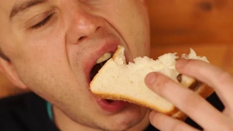 A man bites and eats a sandwich made of white bread. Stock Footage 153783609