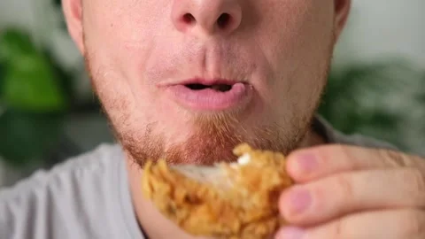 Man bites, chews fried chicken wing in breadcrumbs. man eats fast food Stock Footage 218614613